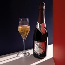 A bottle and a glass of sparkling wine casting a shadow.
