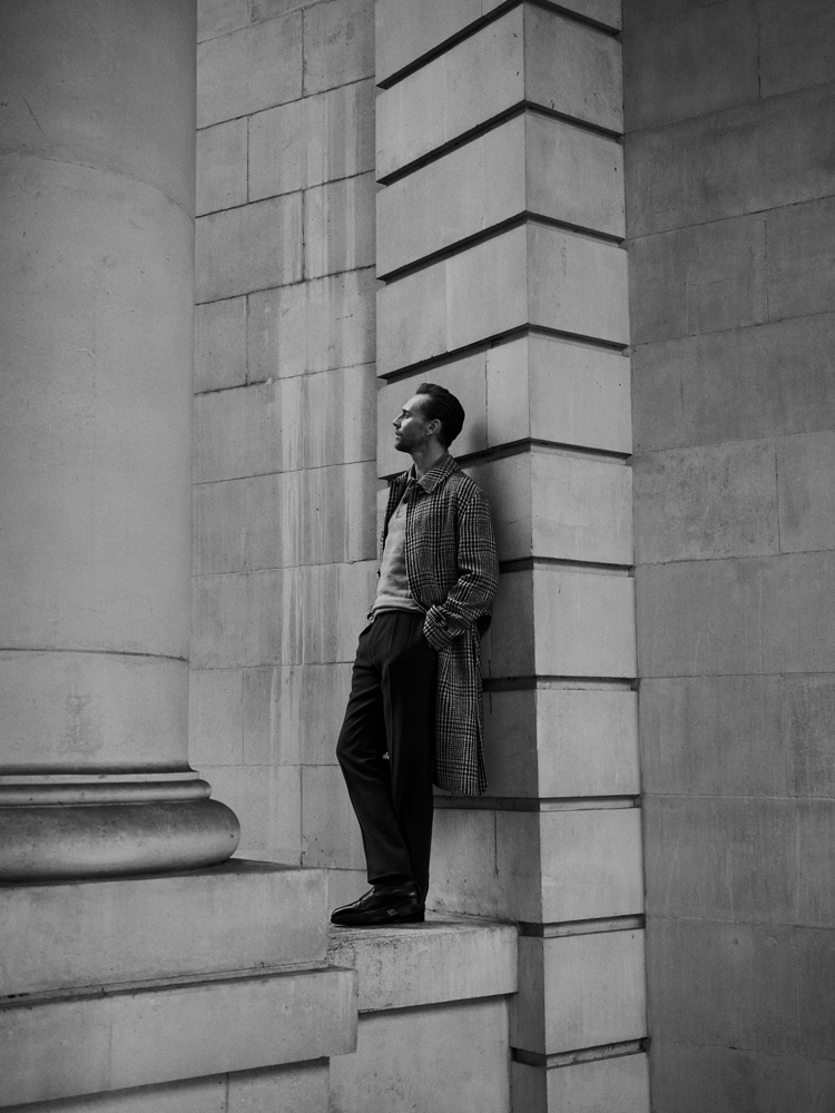 A black and white photograph of Tom Hiddleston leaning against a wall.