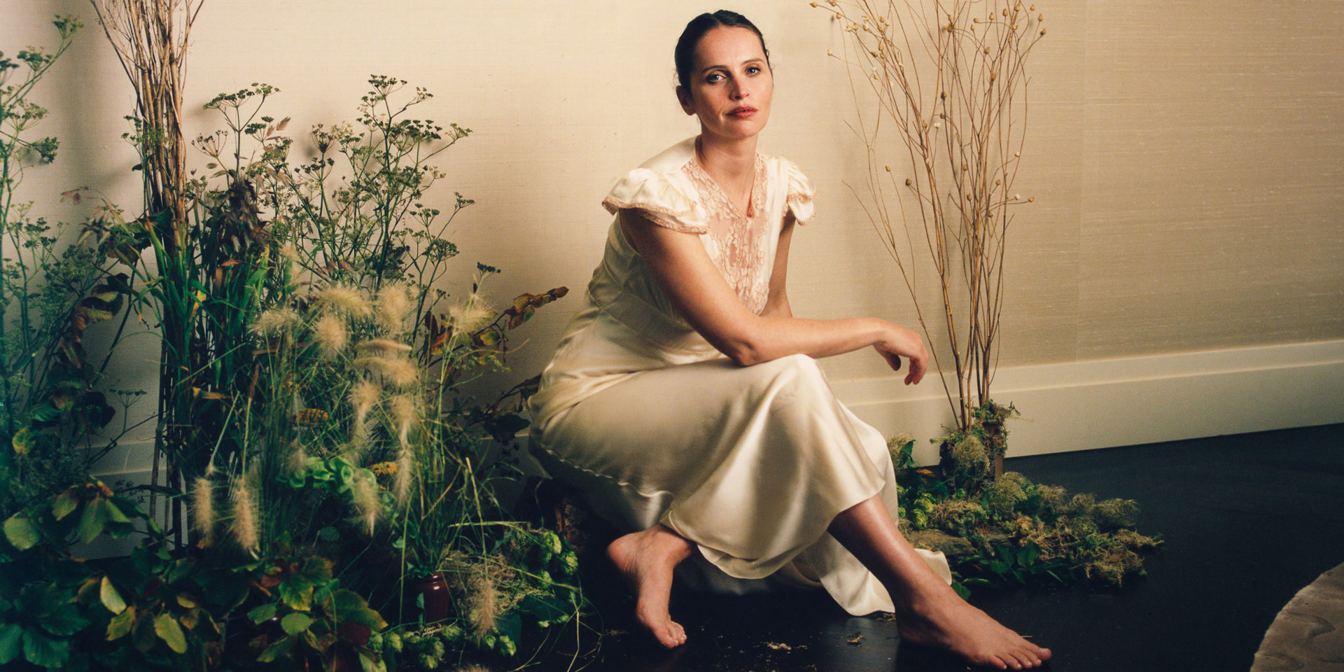 The actor Felicity Jones in a glamorous dress sitting among flowers.