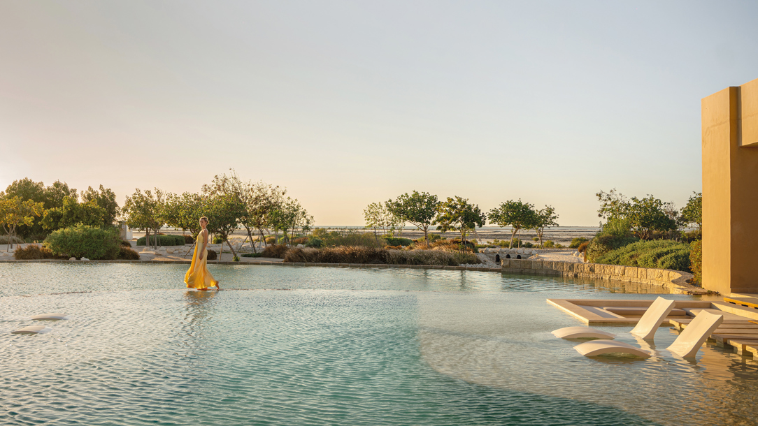 A woman walking across the pool at the at the Zulal Wellness Resort in Qatar.