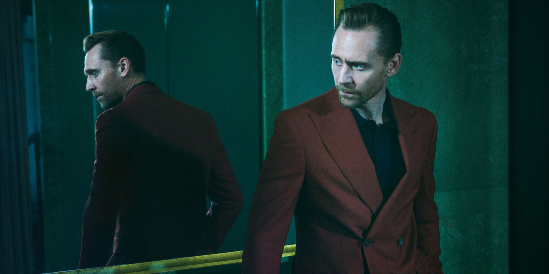 A portrait of Tom Hiddleston standing with his back to a mirror.