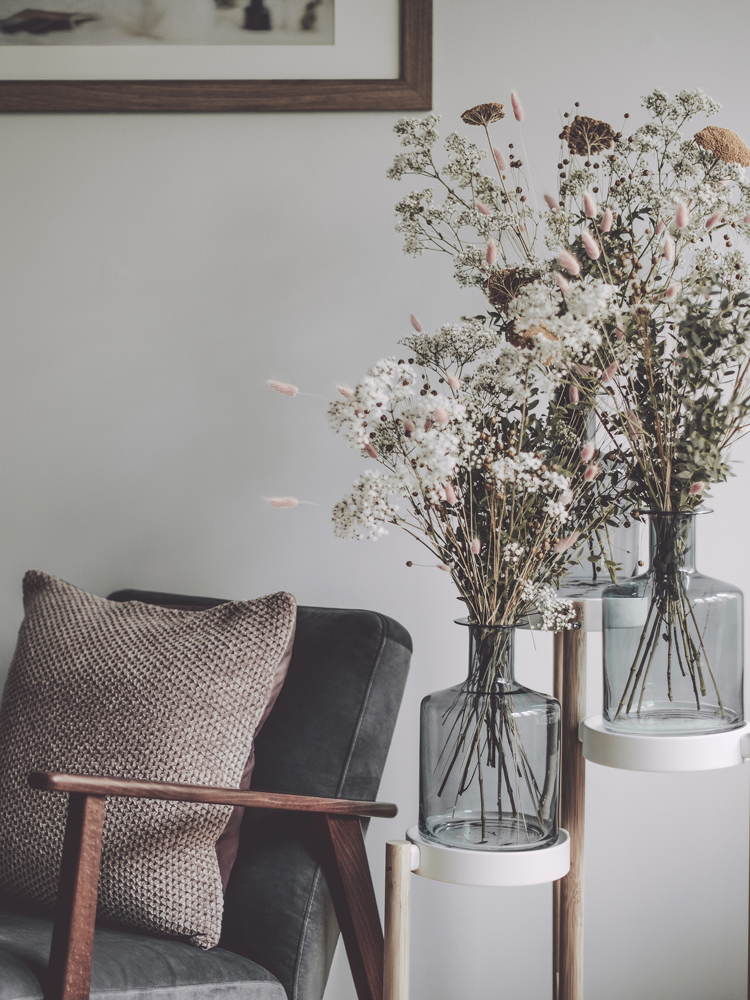 An array of flowers in two glass vases on a side table.