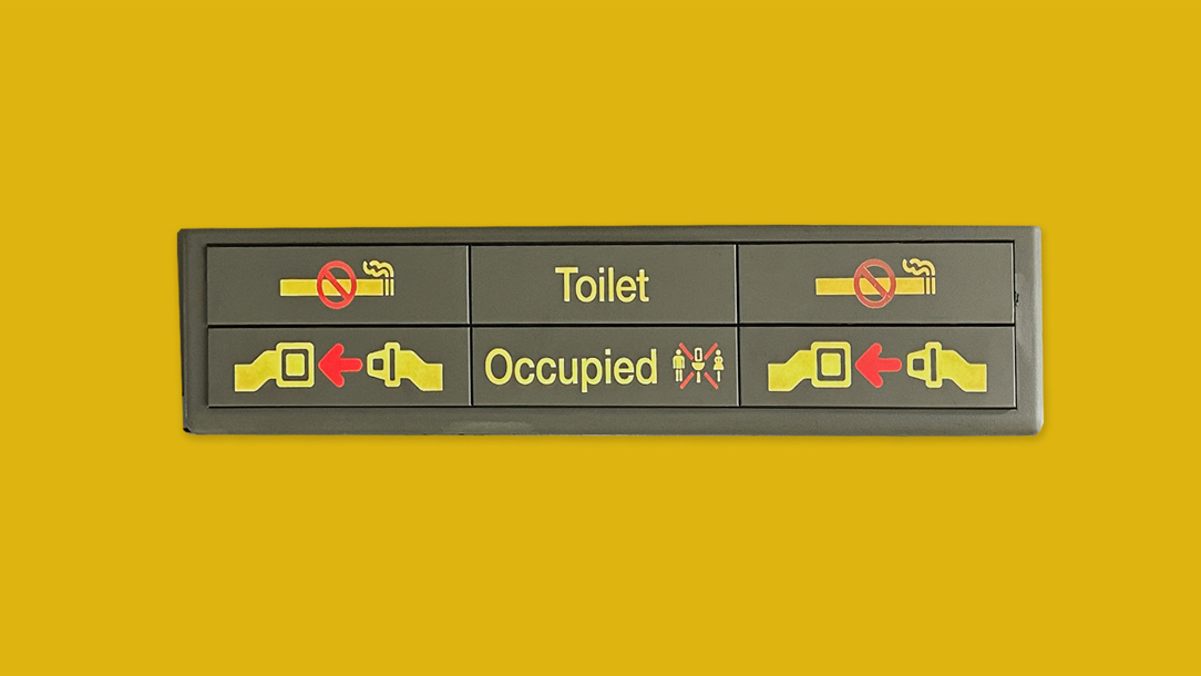 The signage for a toilet door on a plane on a bright yellow background.